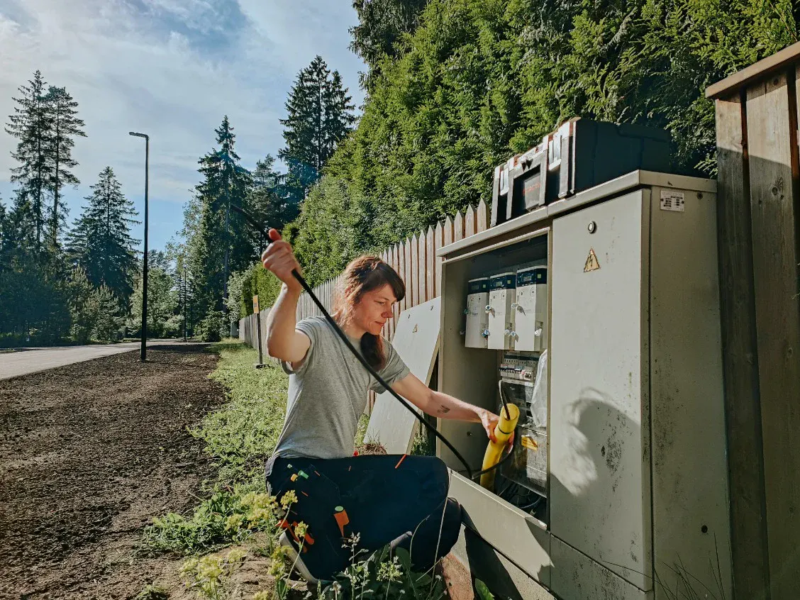 An electrician kneels by an open roadside cabinet and pulls a cable through.