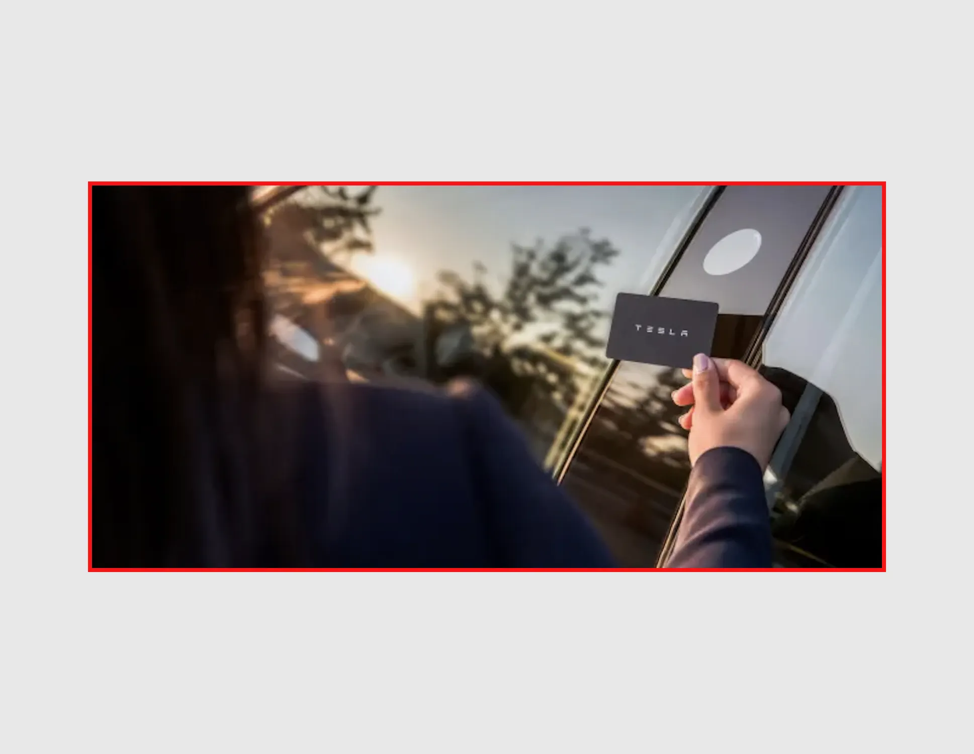 A hand holding a Tesla key card against the car’s window pillar to unlock it